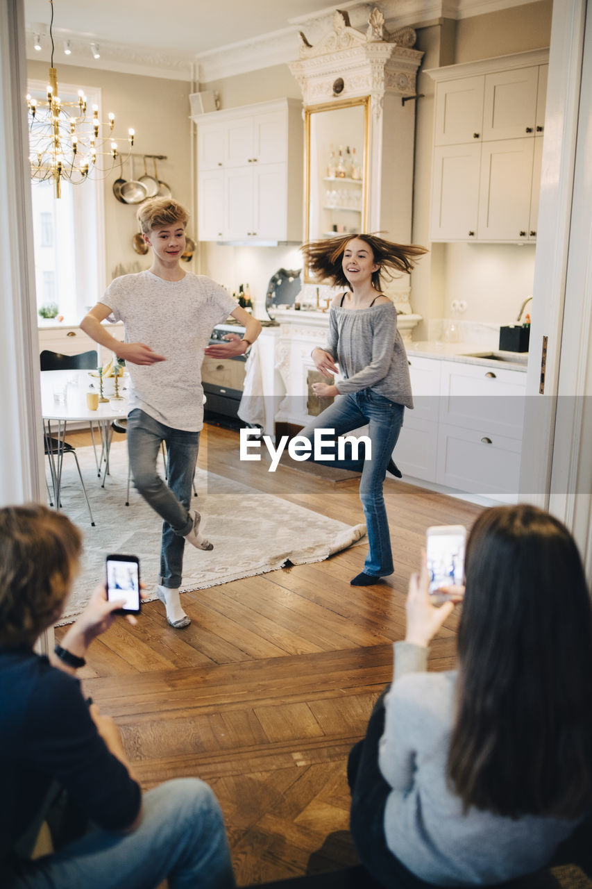 Friends photographing teenage boy and girl dancing at home