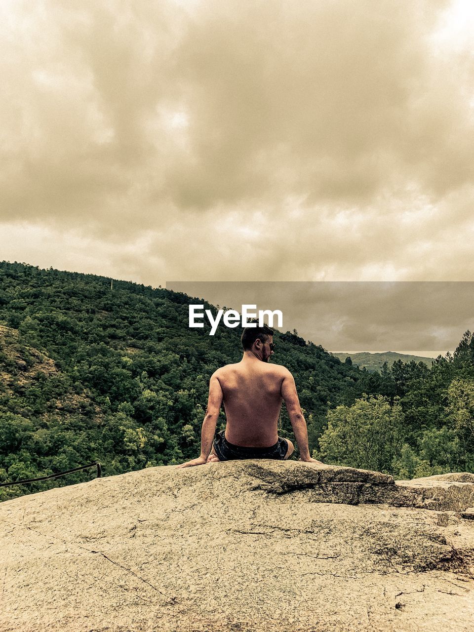 REAR VIEW OF SHIRTLESS MAN STANDING AGAINST SKY