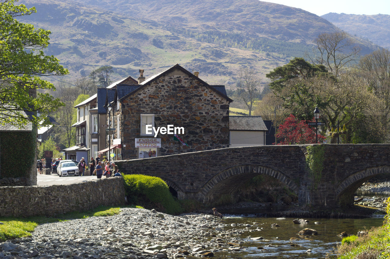 ARCH BRIDGE OVER RIVER BY BUILDINGS AGAINST MOUNTAIN