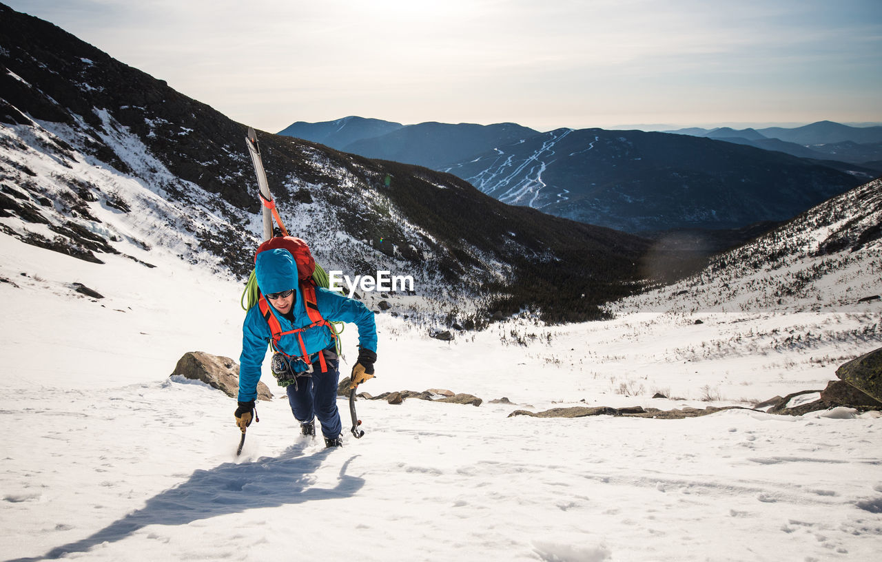 Climber ascending mountain with tools and skis in the white mountains