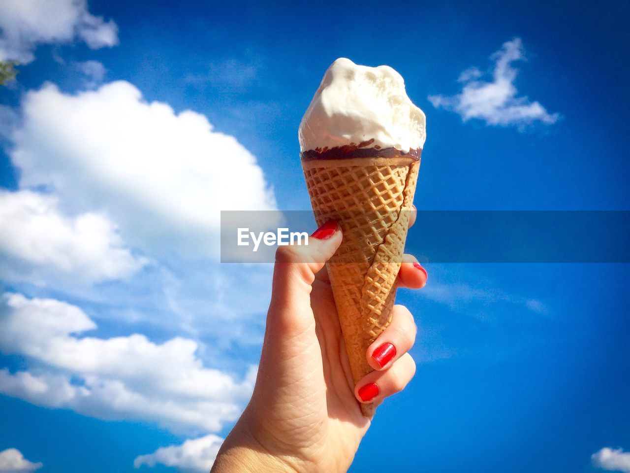 Midsection of woman holding ice cream against blue sky