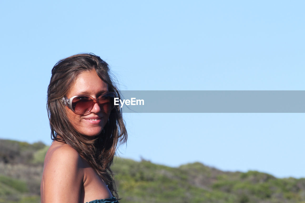 Portrait of woman wearing sunglasses against clear blue sky