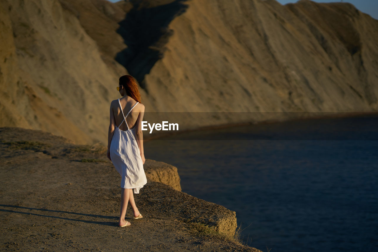 REAR VIEW OF WOMAN STANDING ON ROCK IN SEA