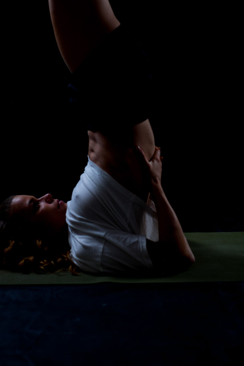 Side view of woman practicing shoulder stand over black background