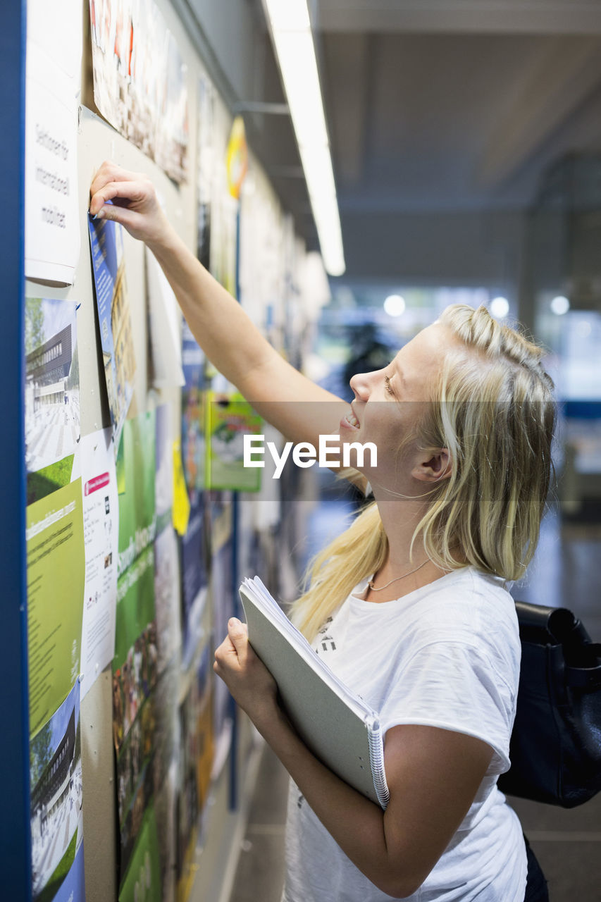 University student tacking paper to bulletin board in college