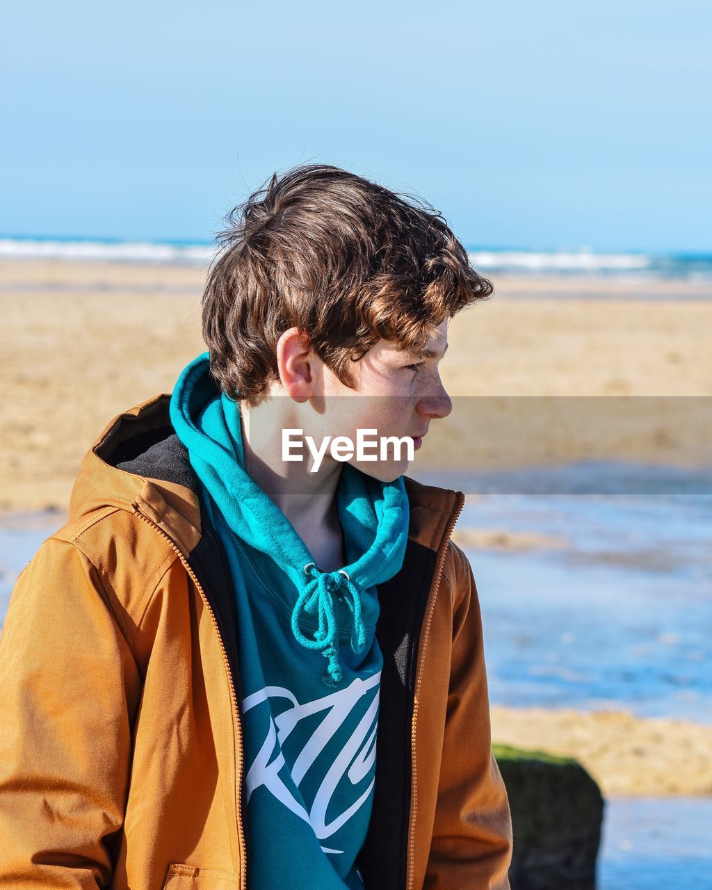 Teenage boy standing at beach against sky