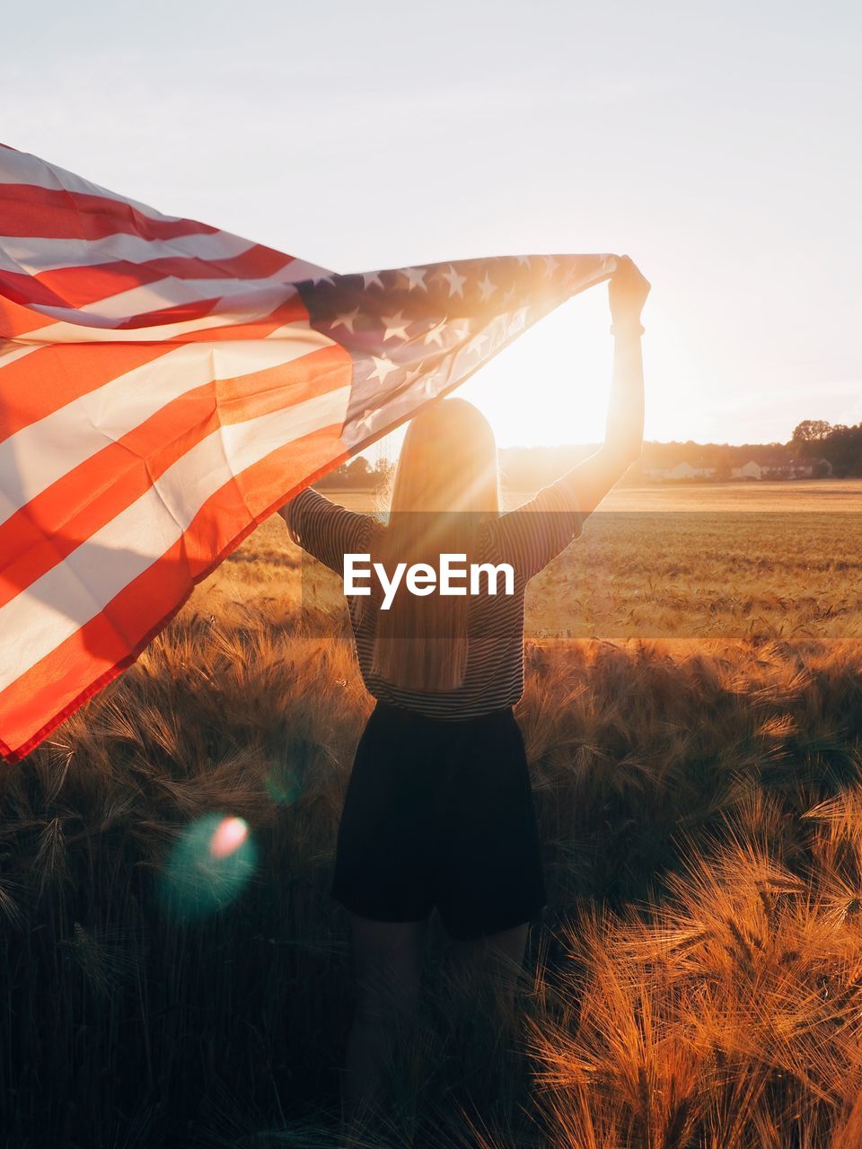 Rear view of woman standing on field against sky during sunset holding us flag 