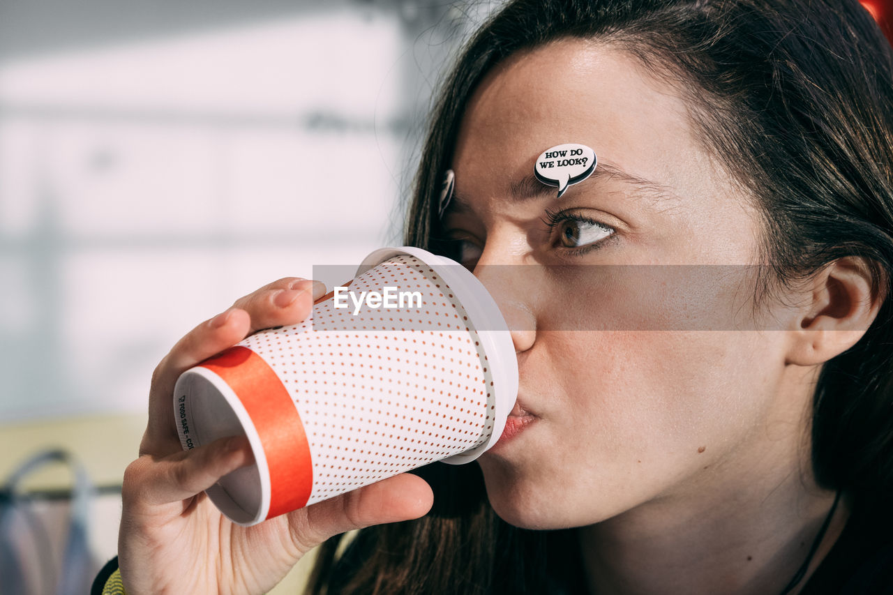 Close-up of young woman with speech bubble on face drinking coffee