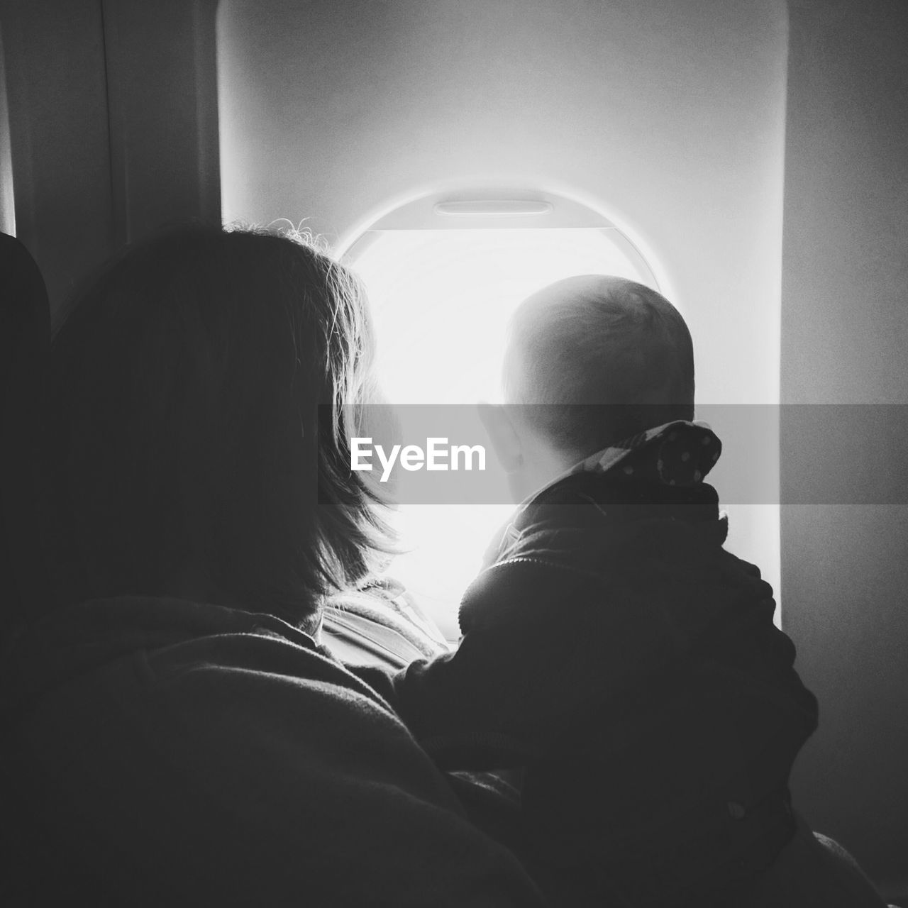 Close-up of mother and son looking through window while traveling in airplane