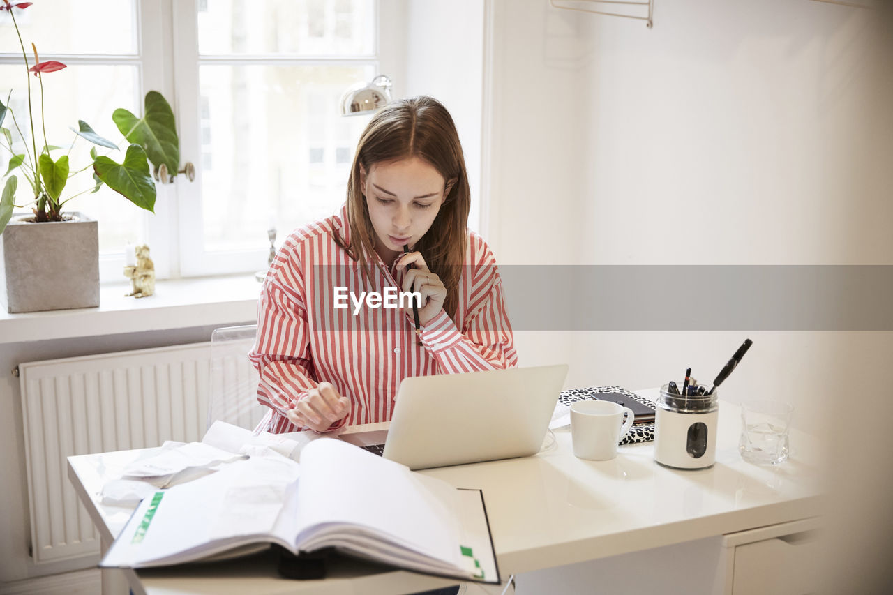 Female accountant using laptop while doing paperwork at home