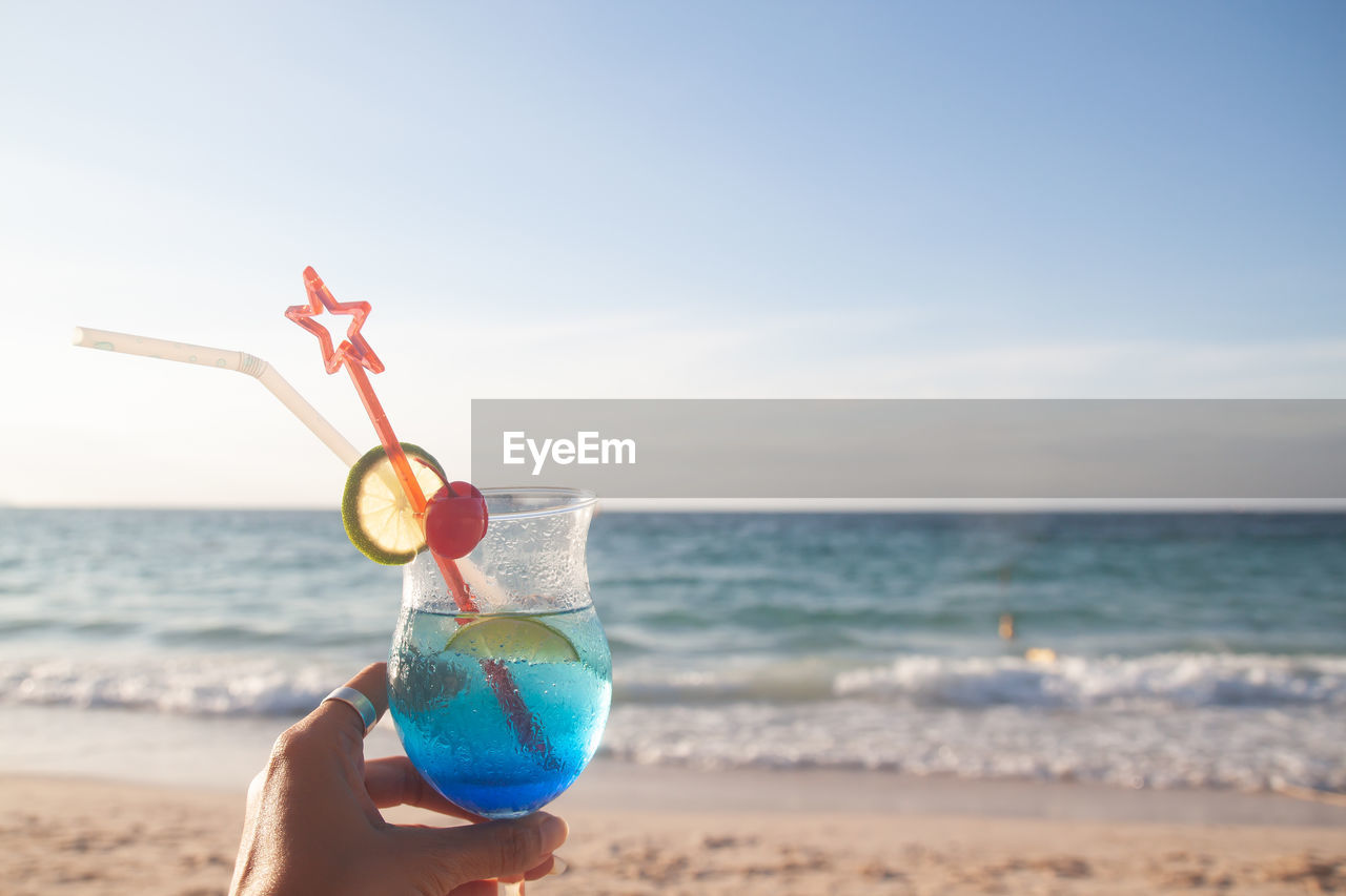 PERSON HOLDING DRINK AT BEACH