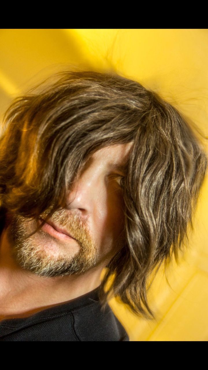 Close-up portrait of young man with long hair against yellow background