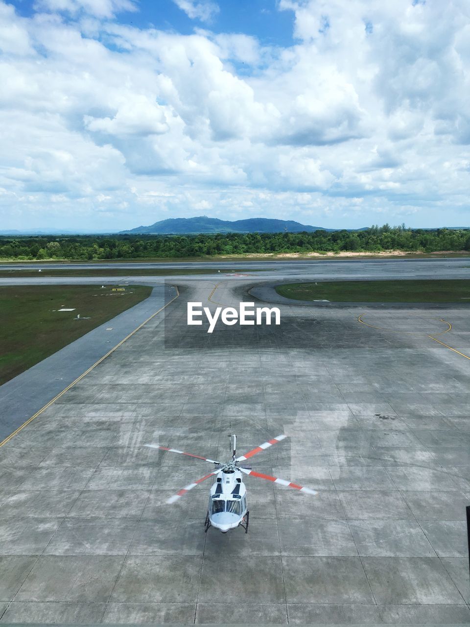 High angle view of helicopter at airport runway against cloudy sky