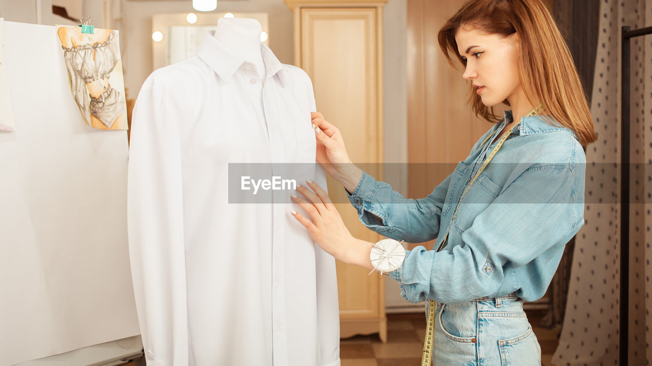 Portrait of seamstress woman in atelier. beautiful room, dummy with white shirt, counter with ready 