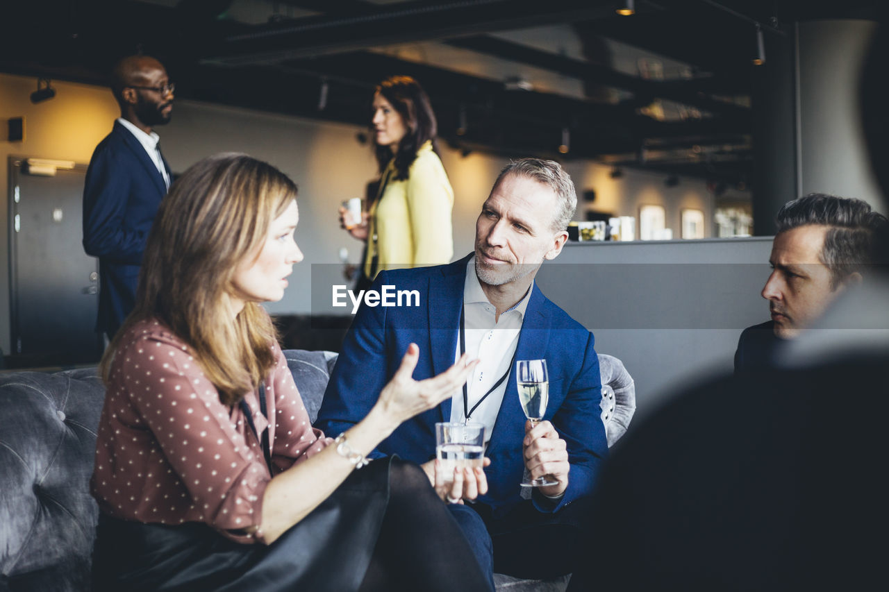 Female professional talking to male colleagues while sitting in office