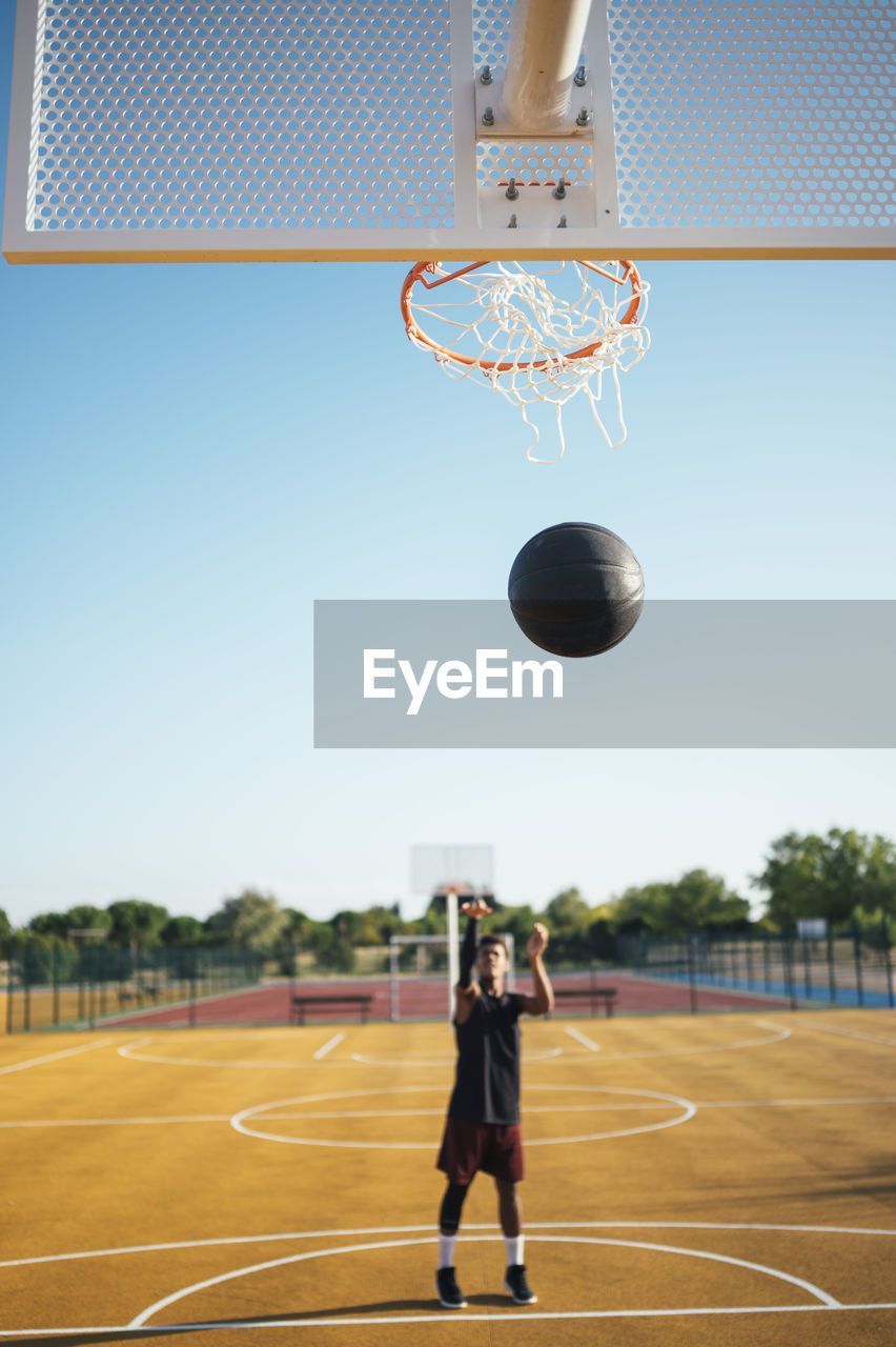 Front view of powerful energetic young african american sportsman playing basketball trying to hit the ball in net on playground