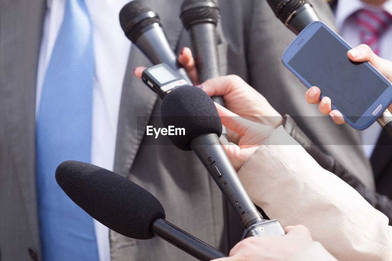 Cropped hand of journalist holding microphone in front of businessman