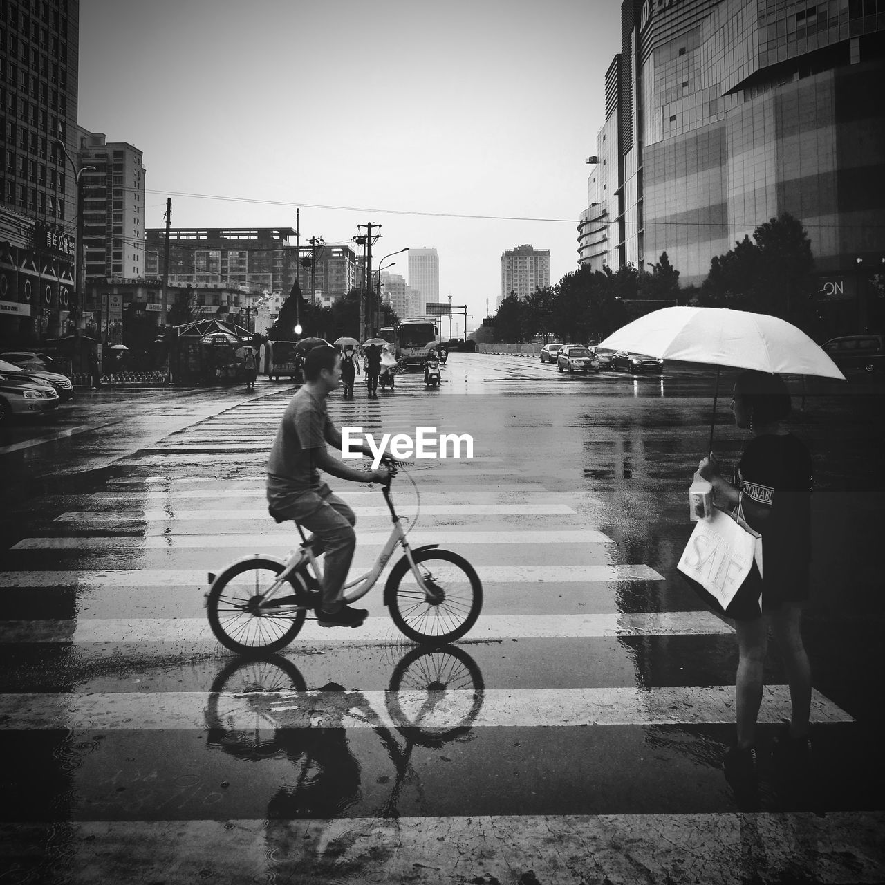 MAN RIDING BICYCLE ON WET ROAD AGAINST SKY