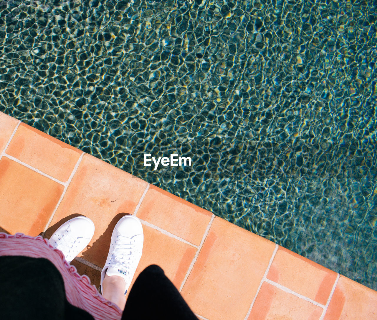 Low section of woman standing in front of swimming pool