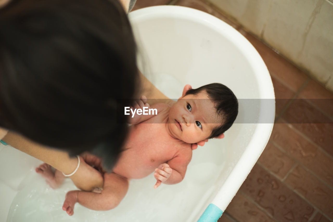 High angle view of mother holding naked newborn daughter in bathtub