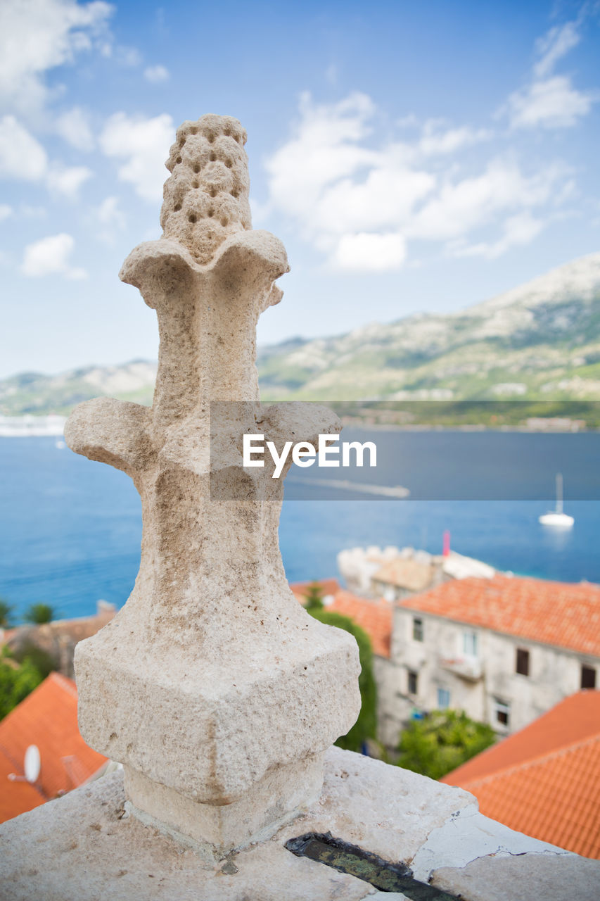 CLOSE-UP OF CROSS SCULPTURE AGAINST SKY