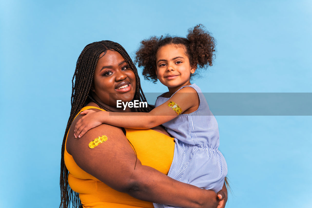 PORTRAIT OF HAPPY MOTHER AND DAUGHTER AGAINST CLEAR BLUE