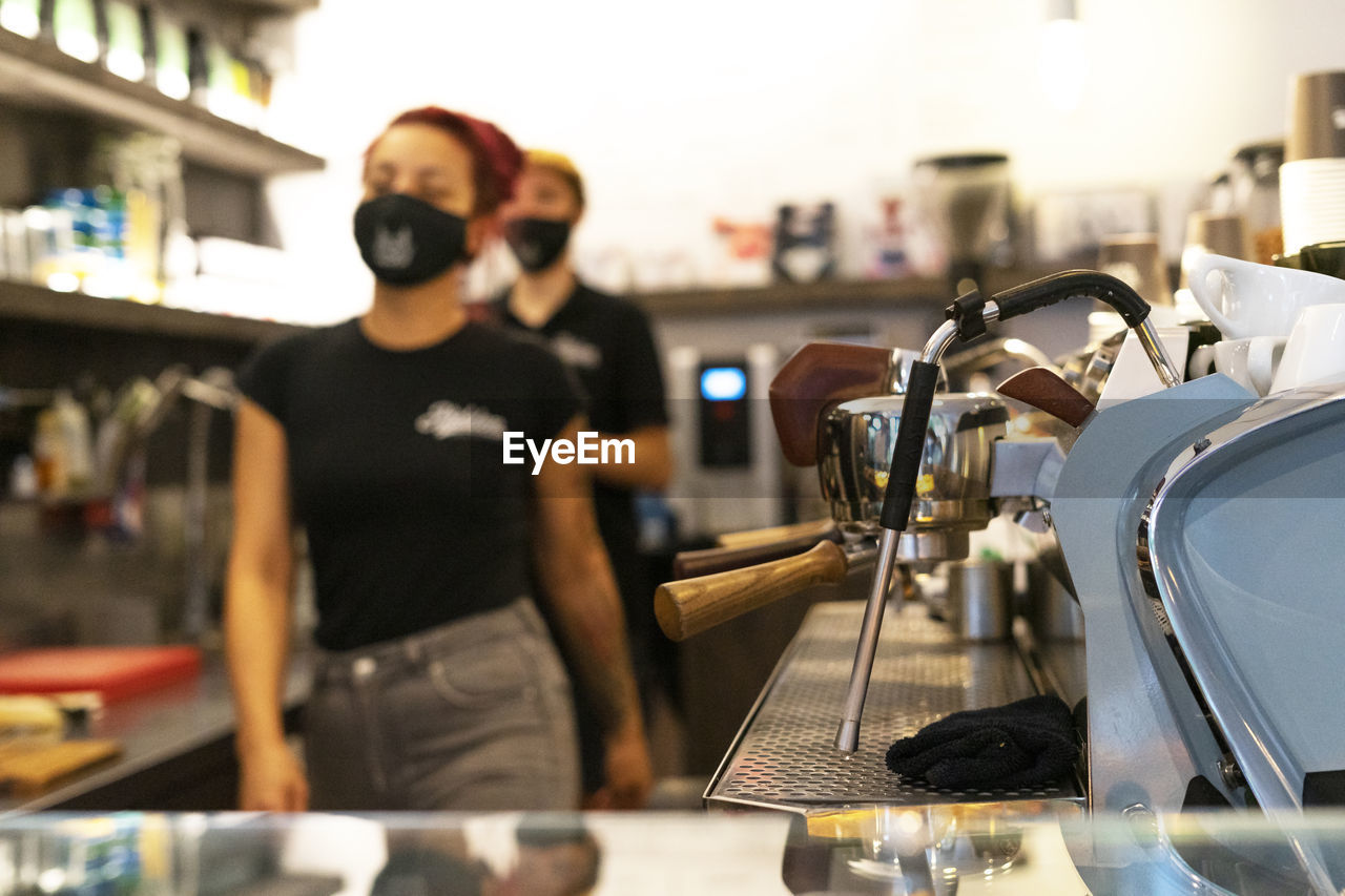 Unrecognizable blurred bartenders in medical masks working in modern coffee shop during covid 19 outbreak