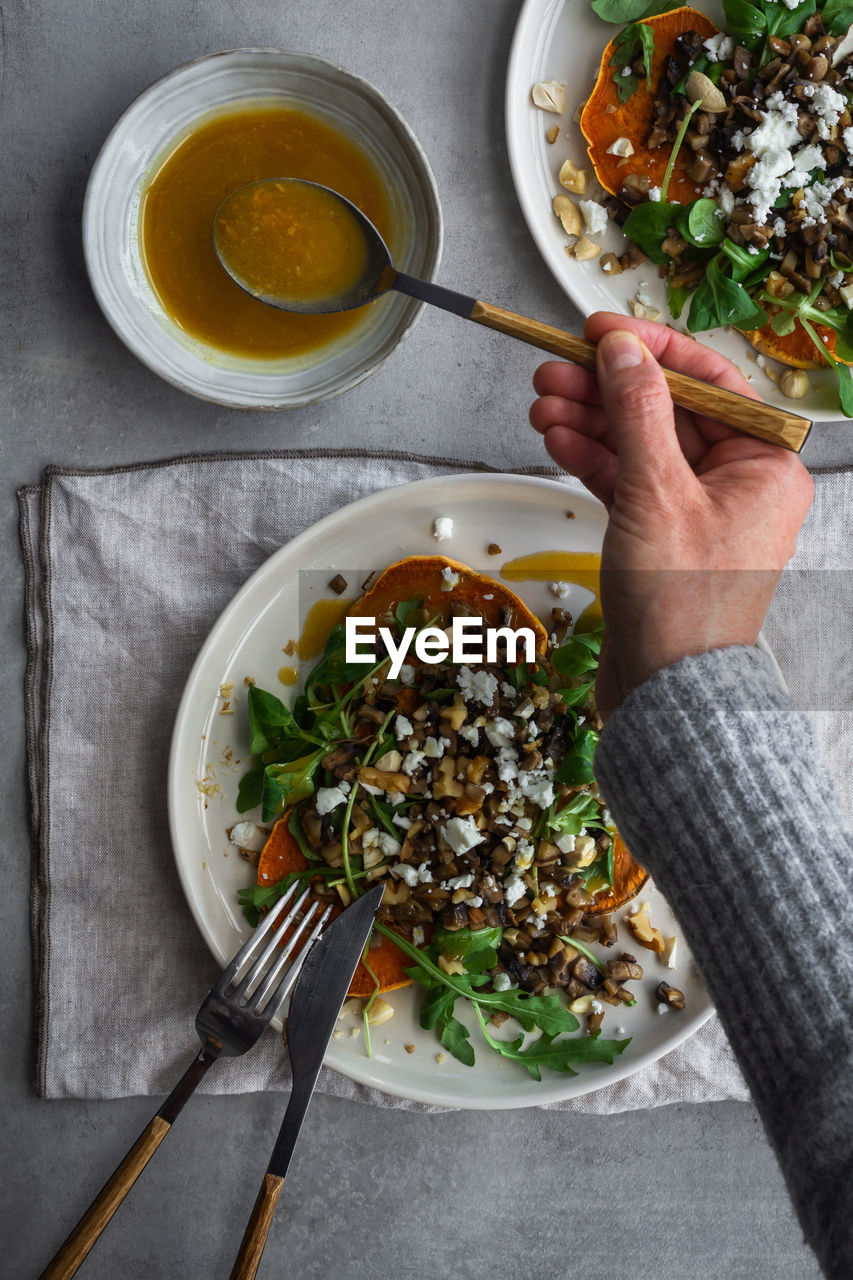 From above unrecognizable person taking spoon of sauce for scrumptious salad while preparing lunch on gray table