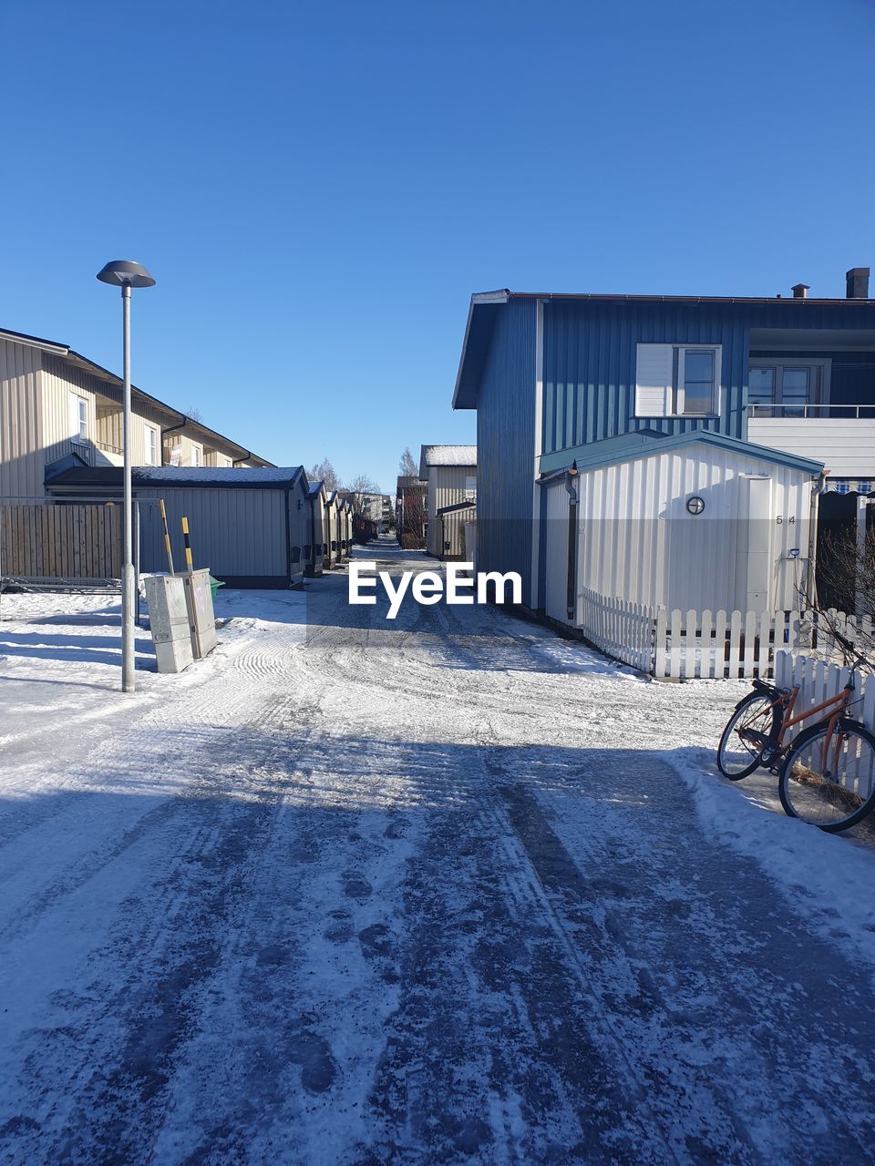 Snow covered street by buildings against clear blue sky