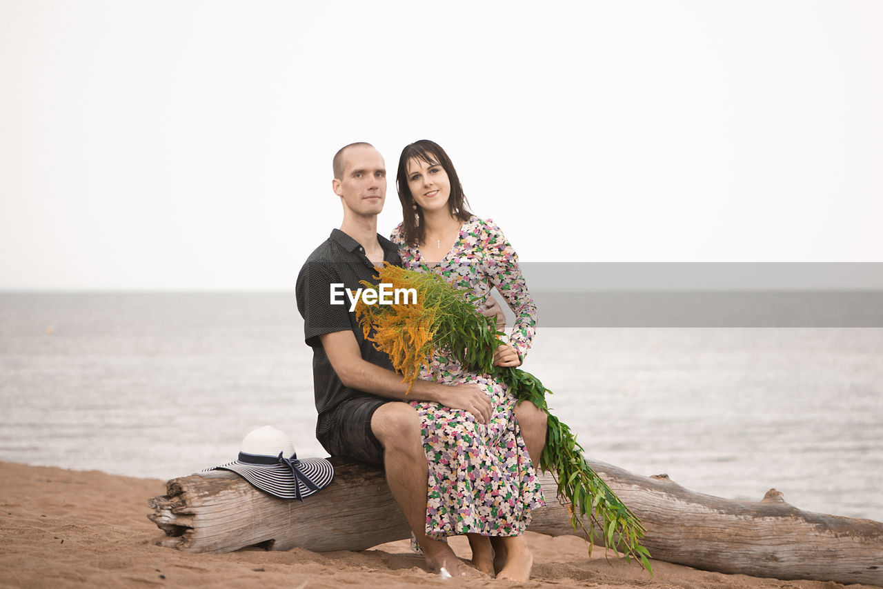 Young romantic couple sitting by the sea and looking to camera