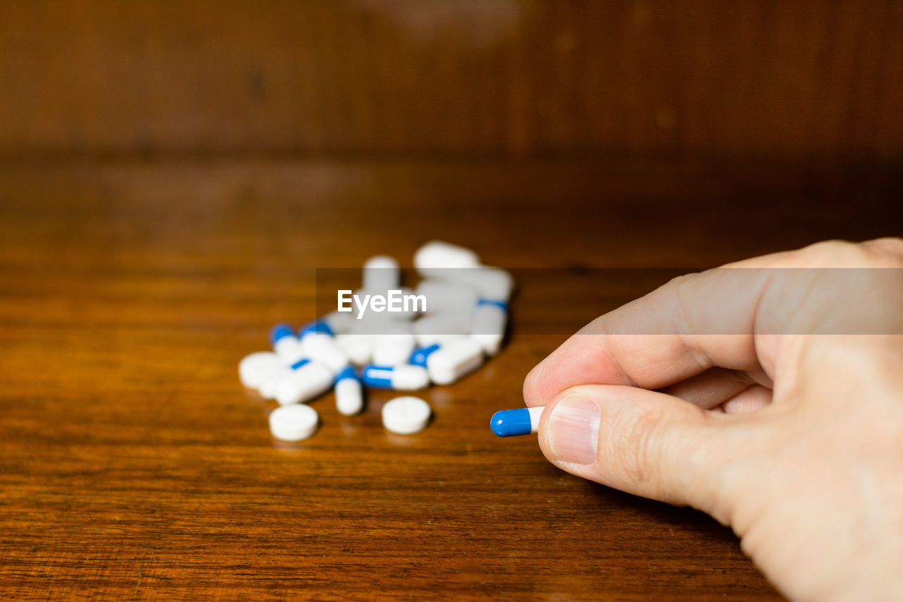 Simple pile of white, blue and yellow pills, medicines, pills stacked on brown background. 