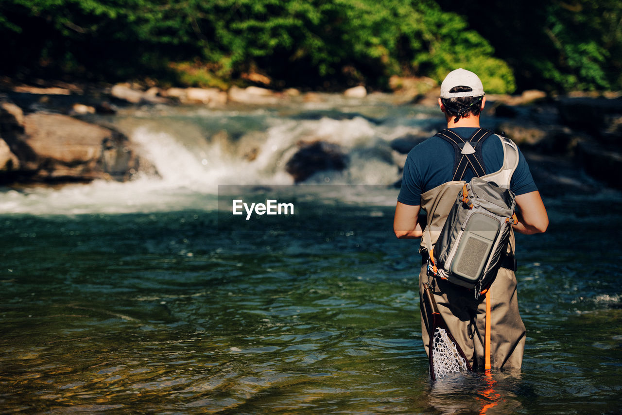 REAR VIEW OF MAN STANDING AT RIVER