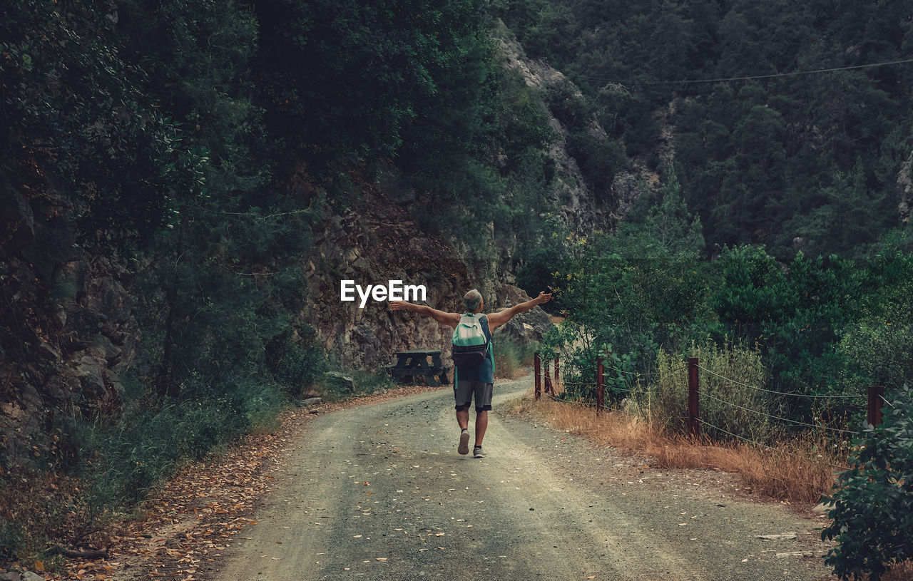 Senior man in the middle of the road in the forrest. hiker in the nature with hands open.