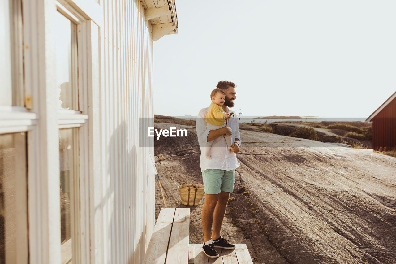 Smiling father with daughter looking away while standing by cabin