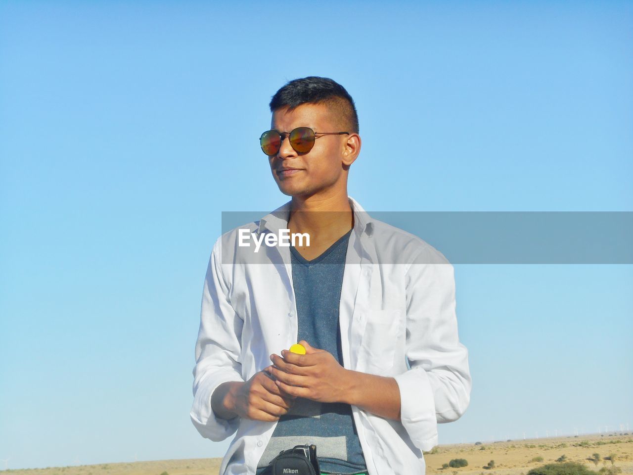 Young man wearing sunglasses standing against clear blue sky