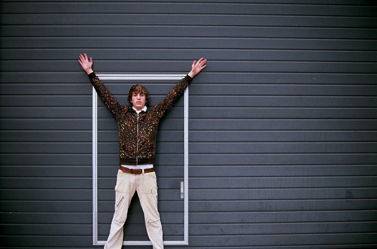 Young man with arms outstretched standing against wall