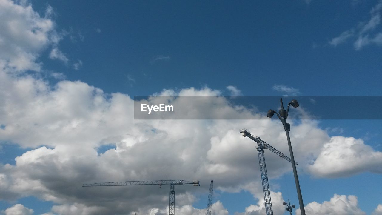 Low angle view of cranes against cloudy sky