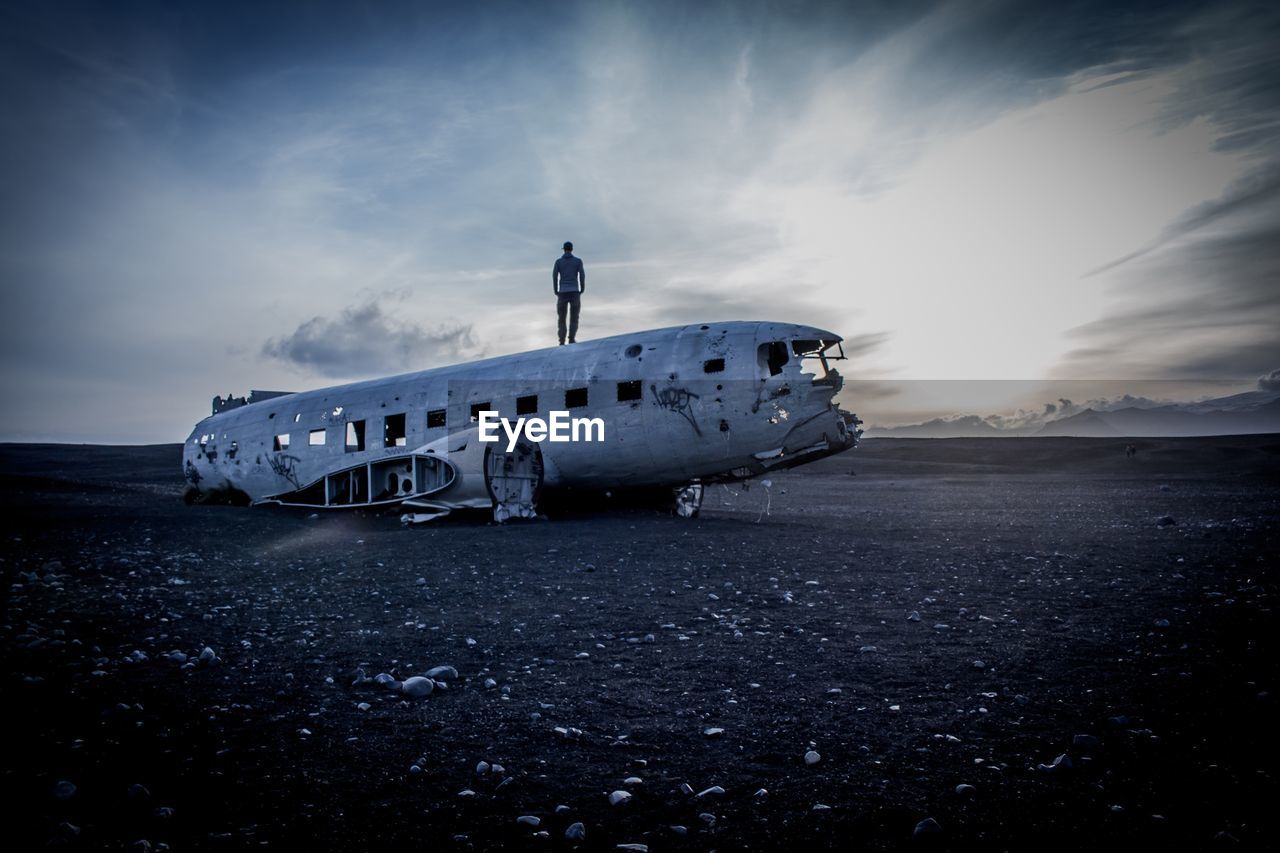 Man standing on abandoned airplane against sky during sunset