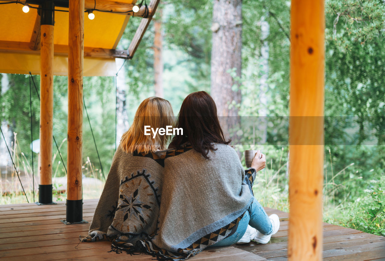 Two young women friends drinking tea and relaxing in glamping in the woods