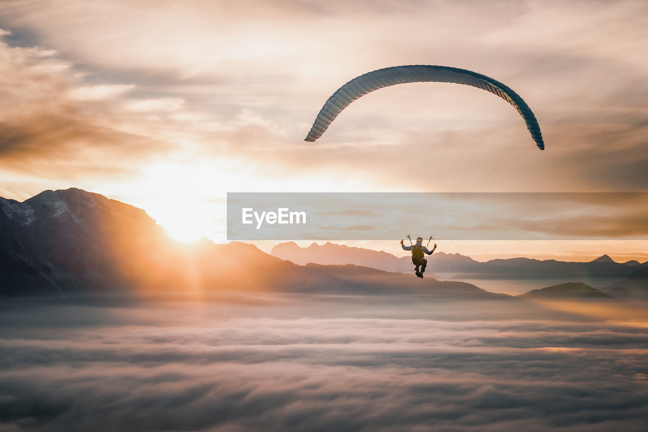 Paragliding pilot flying above sea of clouds at sunset, salzburg, austria.