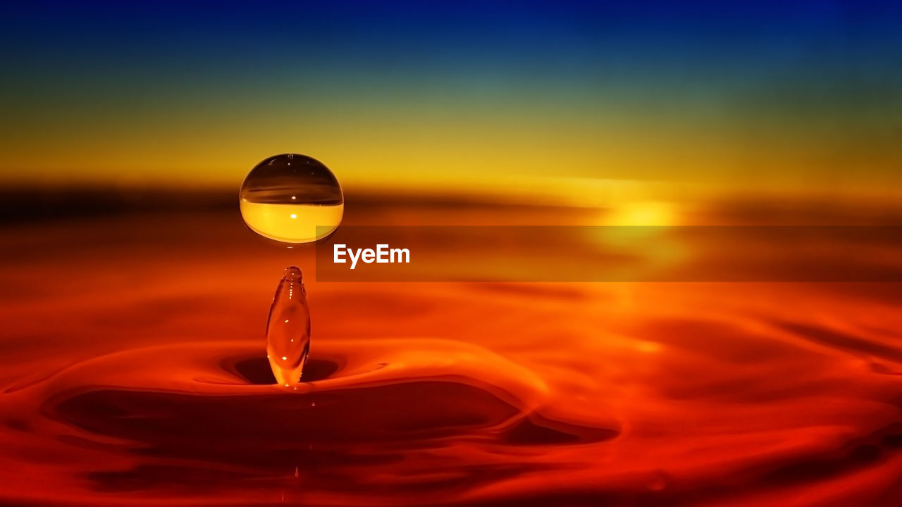 CLOSE-UP OF ILLUMINATED LAMP AGAINST SEA DURING SUNSET