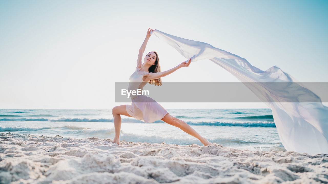 Woman dancing with textile on beach against sky
