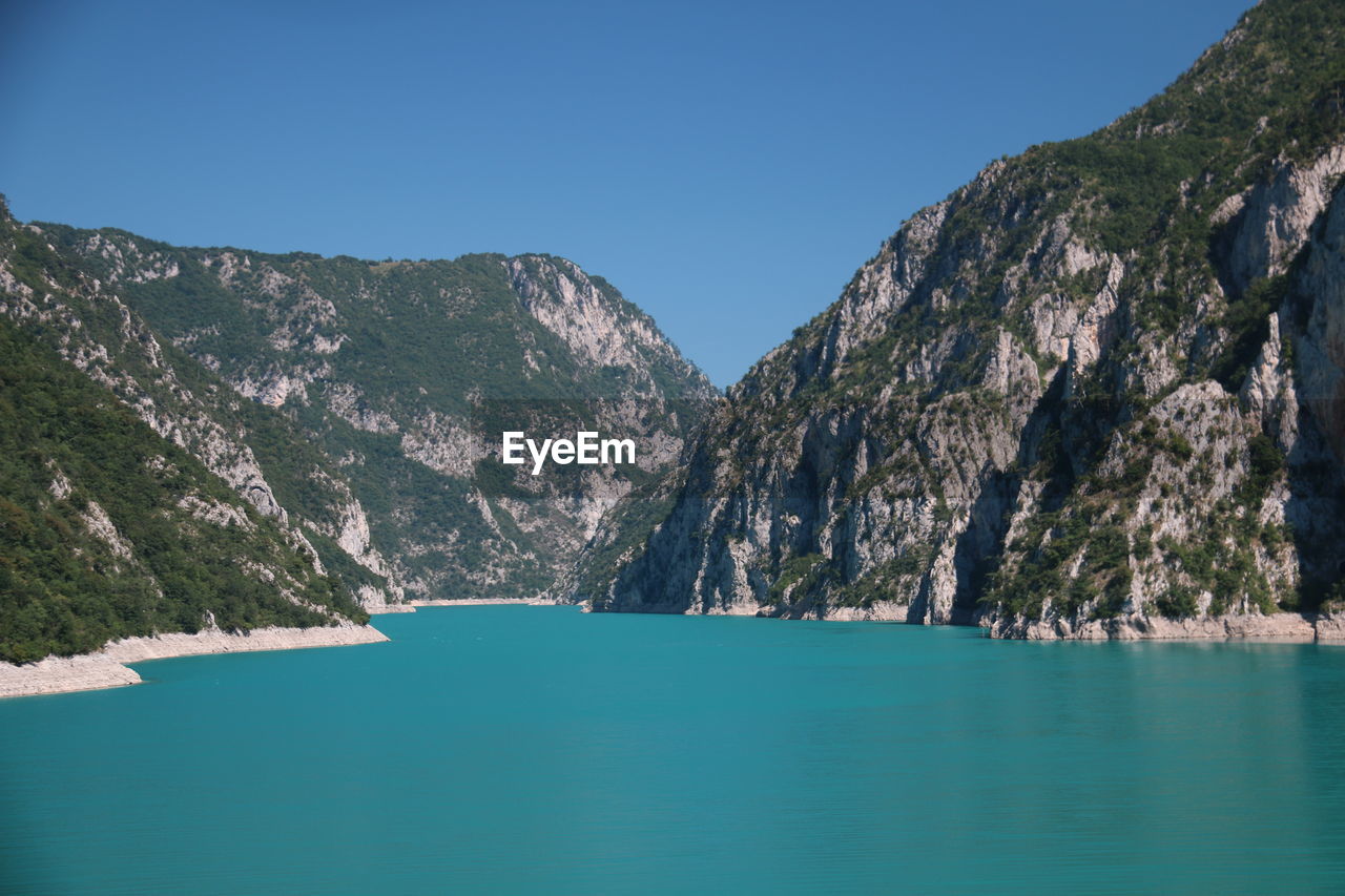 Scenic view of sea and mountains against clear blue sky