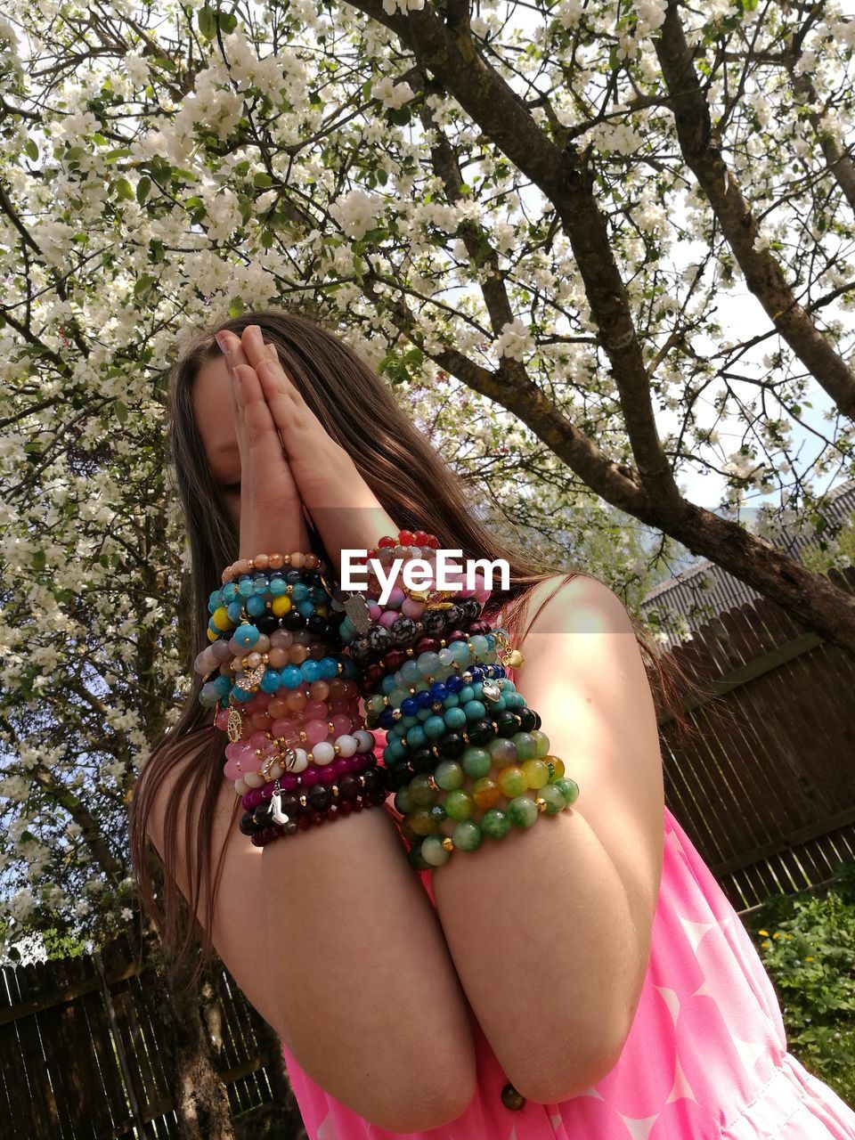 Girl with hands clasped wearing bracelets against trees