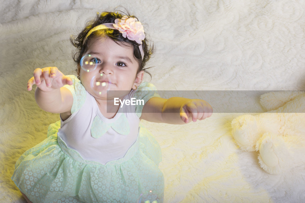 Cute smiling girl playing with bubbles on bed