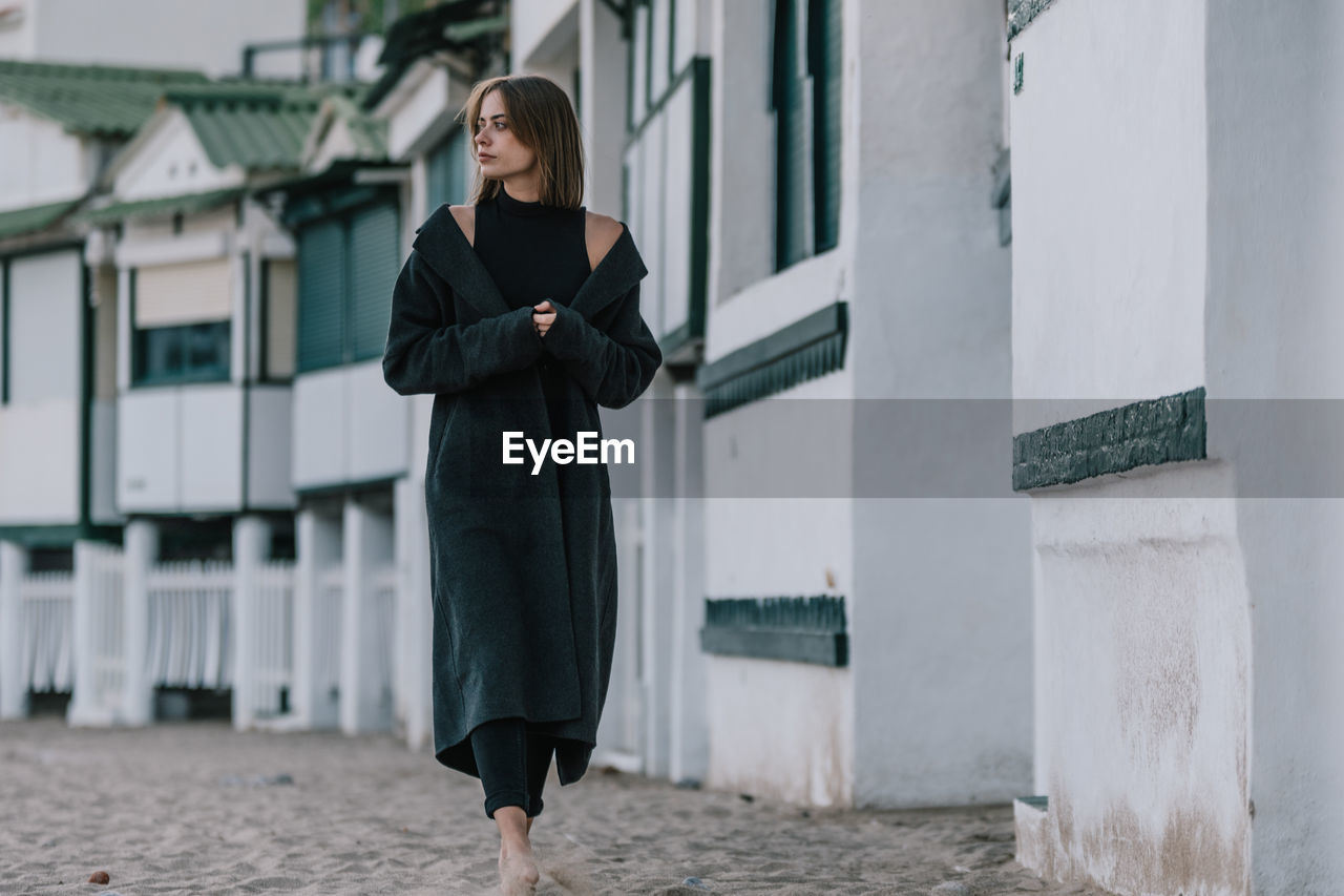 Young lonely female in stylish clothes walking along paved street in ancient city and looking away