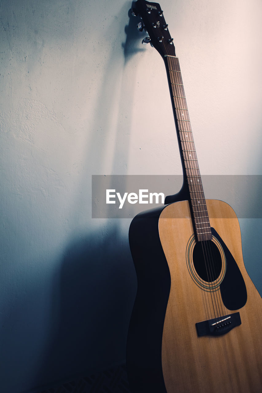 Close-up of guitar against wall at home