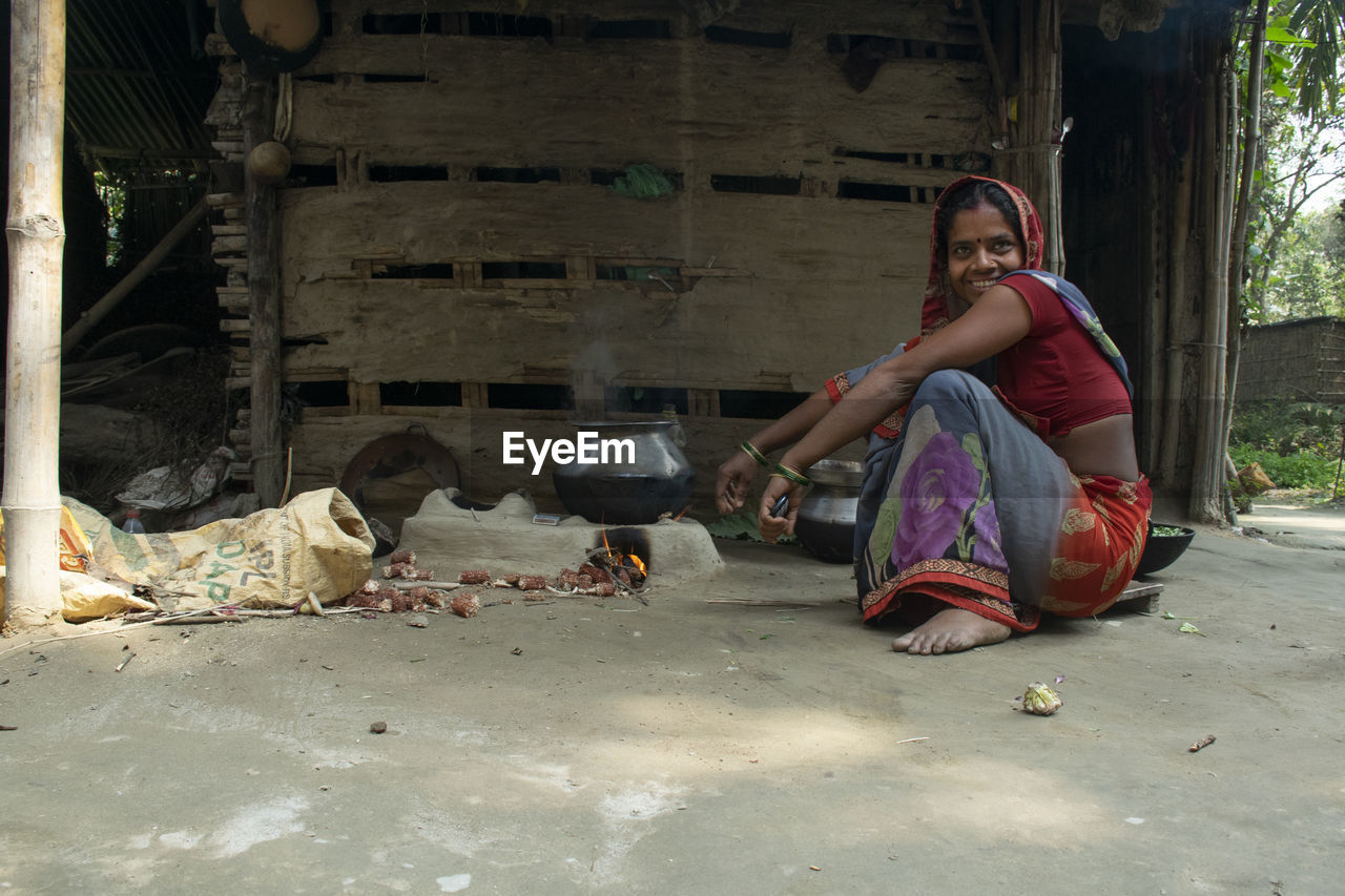 Full length of indian woman sitting outdoors making food on chulha