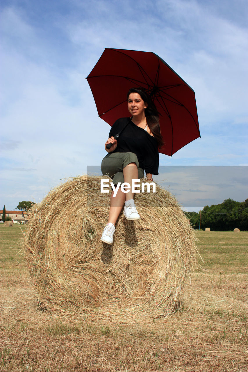 Young woman on a hay ball in a plowed field in tuscany in summer under the umbrella enjoying the sun