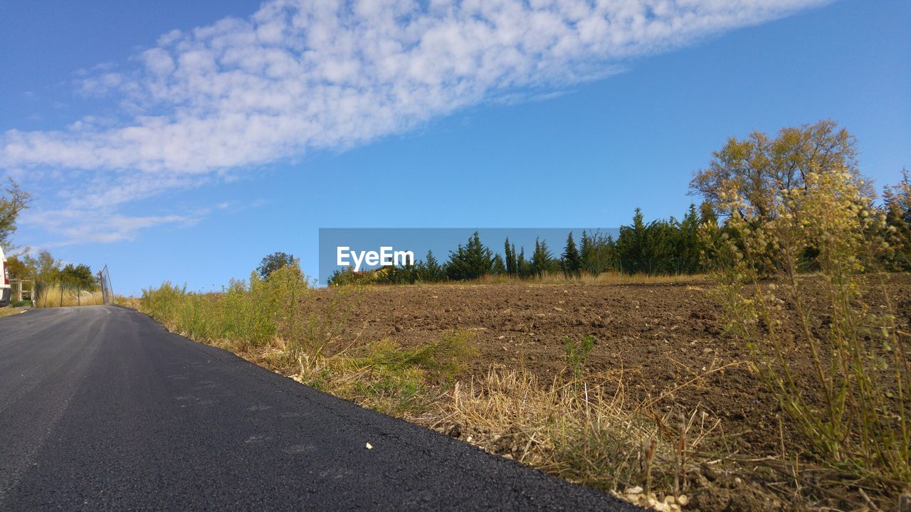 Road amidst field against blue sky